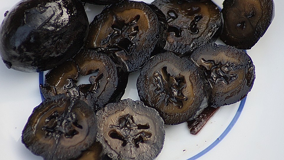 In Scheiben geschnittene Schwarze Nüsse mit glänzend dunkler Oberfläche auf einem weißen Teller